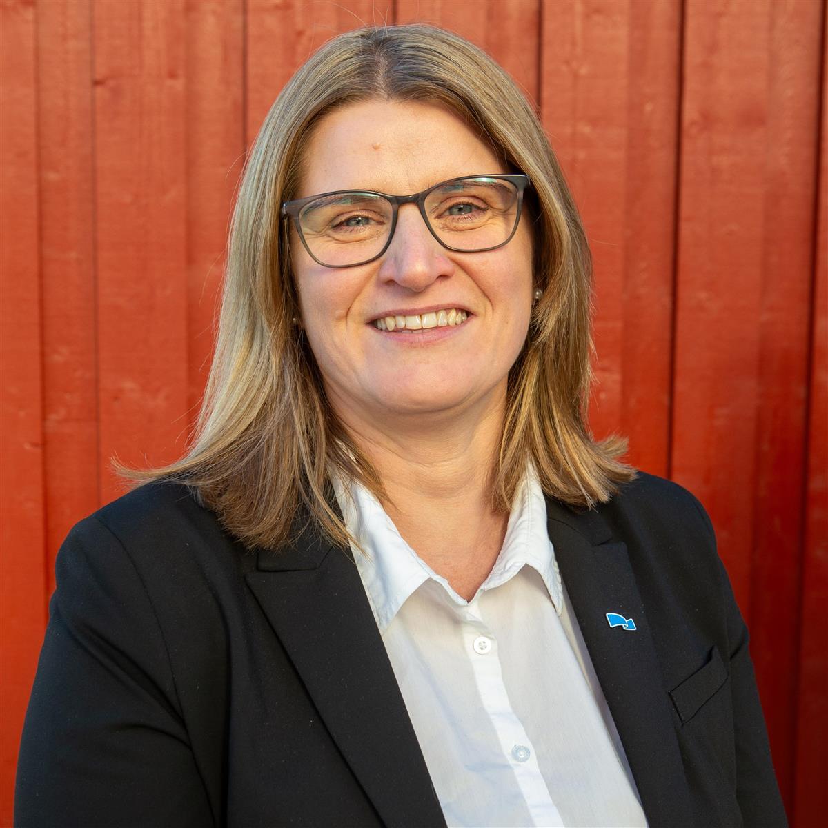 Portrett av smilende kvinne foran rød vegg. - Klikk for stort bilde