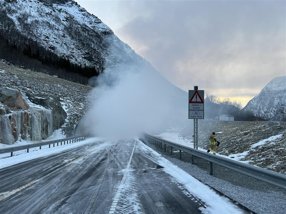 Snødekt veg, tett røyk kommer ut av tunnel.  Et skilt som kan varsle syklist i tunnelen, trykk på knapp.  - Klikk for stort bilde