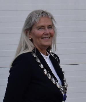 Smilende kvinne med ordførerkjede, foran grå vegg. - Klikk for stort bilde