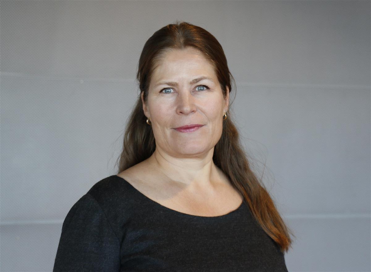 Kvinne med langt hår foran grå vegg, Foto. - Klikk for stort bilde