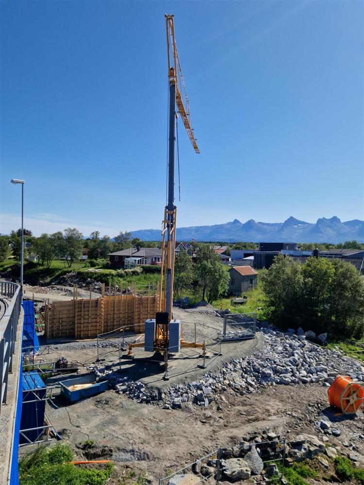 Anleggsarbeid til ny bru. Høy kran.  Sommer. Fjellrekke langt i bakgrunnen. Foto. - Klikk for stort bilde