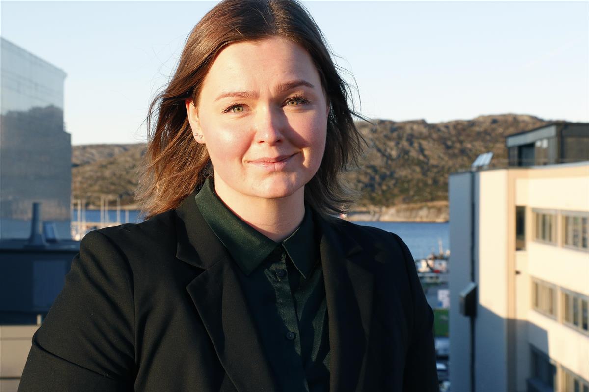 Portrett av lett smilende kvinne. Sjø og fjell i bakgrunnen. - Klikk for stort bilde