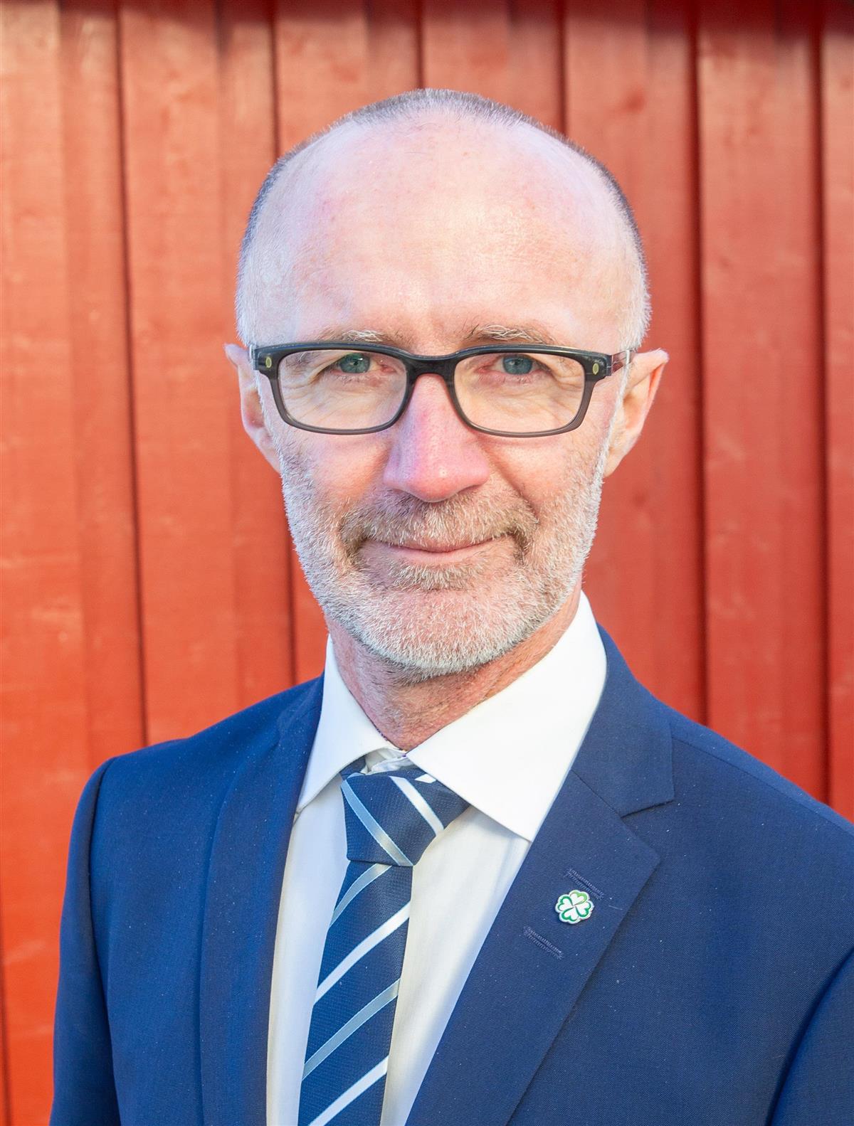 Mann kledd i blå dress foran rød vegg - Klikk for stort bilde