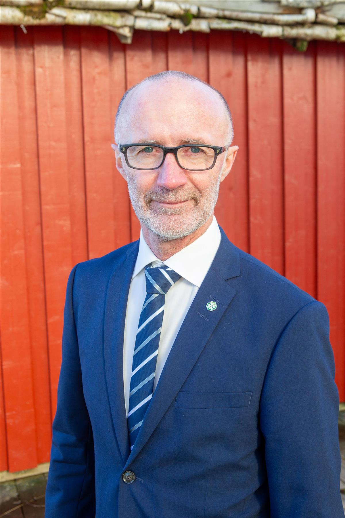 Mann kledd i blå dress foran rød vegg - Klikk for stort bilde