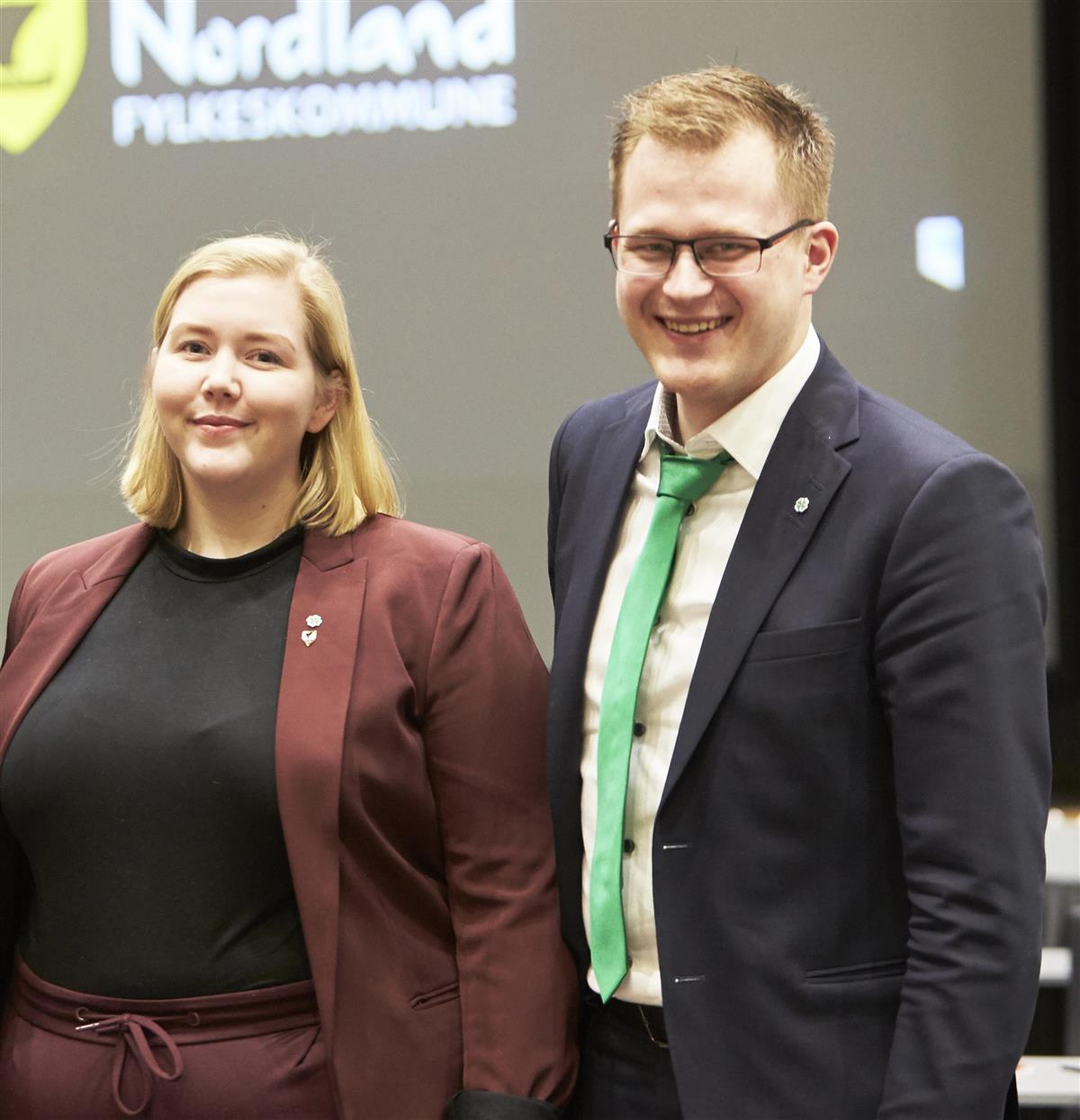 smilende mann og kvinne med en nfk-logo o bakgrunnen. Foto. - Klikk for stort bilde