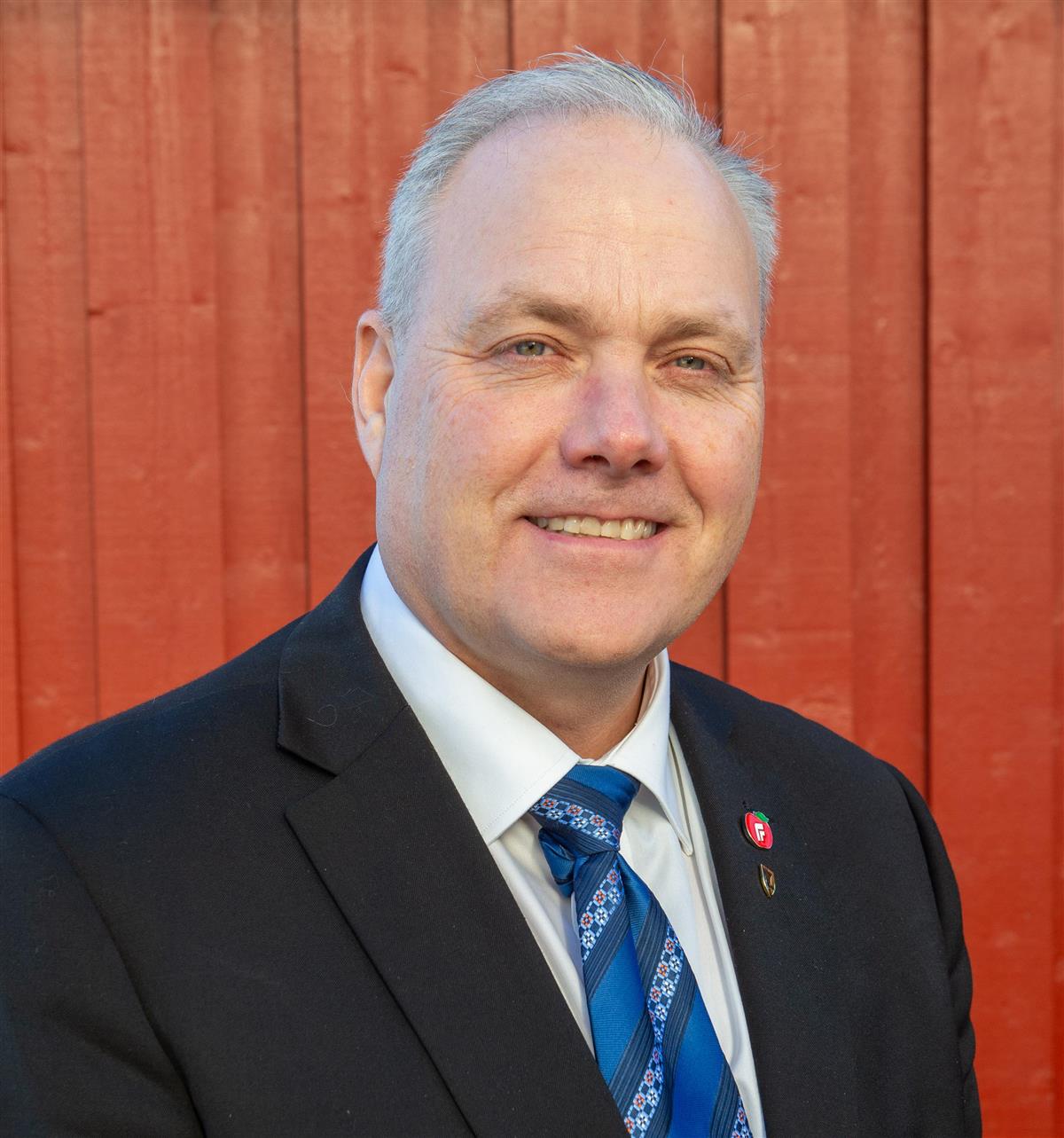 Smilende mann med rød vegg i bakgrunnen. Foto. - Klikk for stort bilde