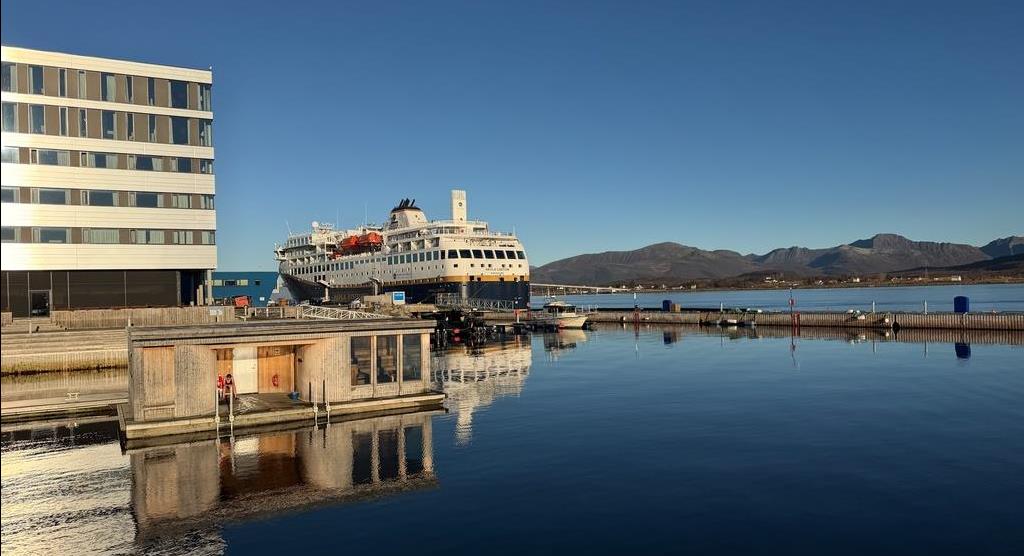 Bilde av ei havn med brygge, bastu, hotellbygg og stort skip. - Klikk for stort bilde