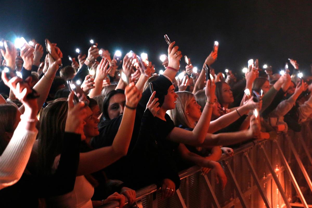 Ungdom i konsertlokale med tente mobiltelefon-lykter. Foto. - Klikk for stort bilde