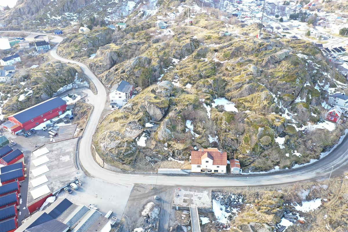 Smal, svingete veg gjennom næringsområde. Steiner, knauser, noe snø. Dronefoto. - Klikk for stort bilde