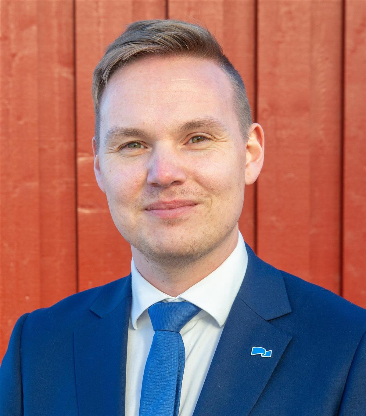 Smilende mann foran en rød vegg. Foto. - Klikk for stort bilde