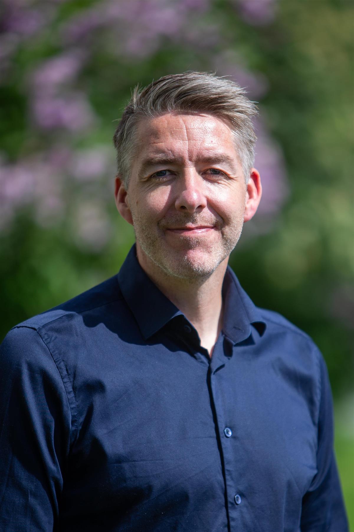 Smilende mann i blå skjorte. Foto - Klikk for stort bilde