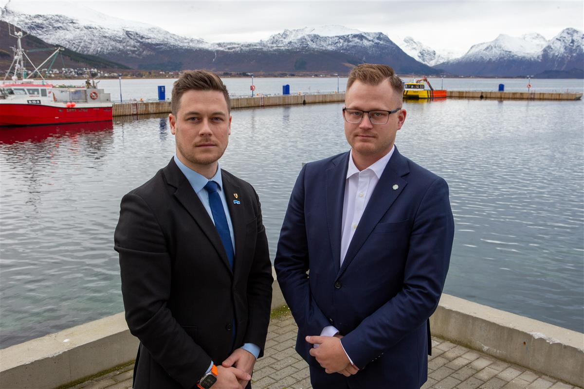 To menn på ei kai med hav og fjell i Bakgrunnen. - Klikk for stort bilde