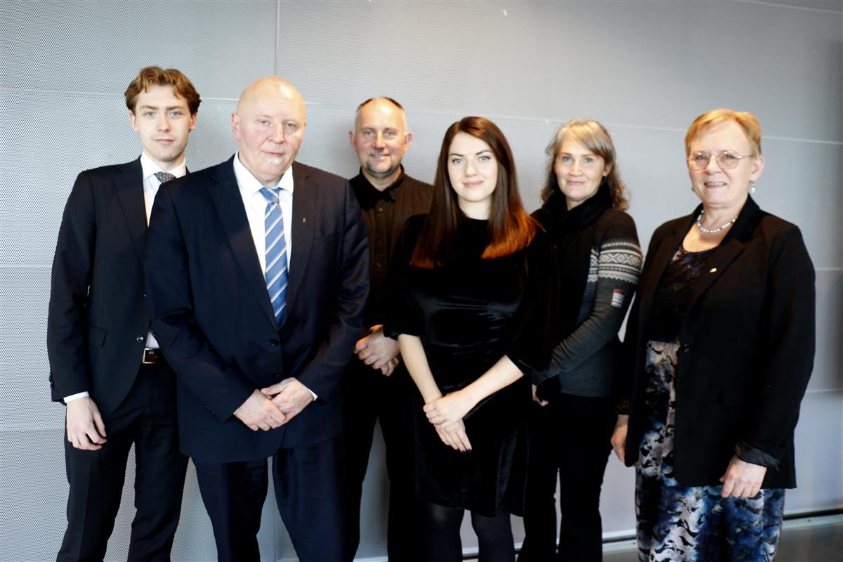 Seks personer framfor en grå vegg, Foto. - Klikk for stort bilde